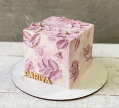 a pink cake with flowers on it sitting on top of a white plate and wooden table