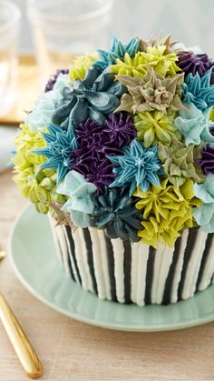 a cupcake decorated with blue, green and purple flowers on a plate next to gold forks