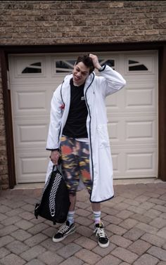 a man standing in front of a garage door with his hand on his head and holding a bag