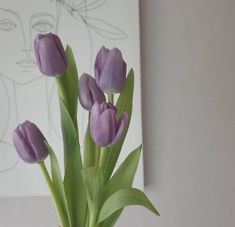 purple tulips are in a vase on a table next to a framed drawing