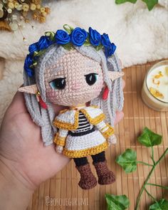 a crocheted doll is holding it's hand in front of a plant