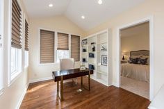 an empty room with a desk and bookcases in front of the window is lit by recessed lights