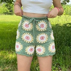 a woman standing in the grass with her hands on her hips and wearing shorts that have crocheted flowers