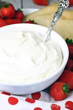 a white bowl filled with whipped cream next to sliced strawberries and bread on a table