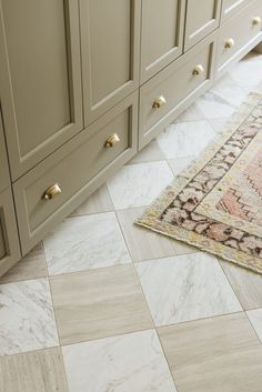 a kitchen with beige cabinets and white marble flooring on the tile, along with a pink area rug