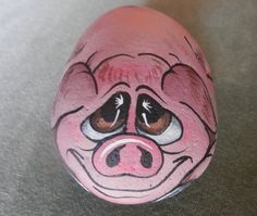 a painted rock with a pig's face on it, sitting on the ground