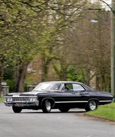 an old black car driving down the street