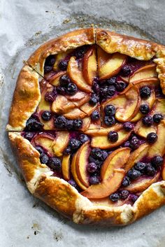 a pie topped with blueberries and peaches on top of a piece of parchment paper