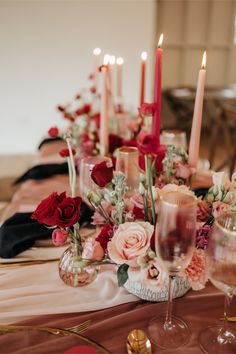 a table topped with lots of pink and red flowers next to tall candle holders filled with wine glasses