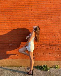 a woman standing in front of a brick wall with her hands on her hips and looking up