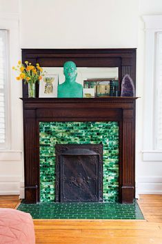 a fireplace in a living room with green tiles on the mantle and wood flooring