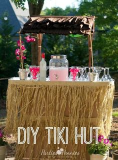 a tiki hut is set up with pink flowers and drinks in front of it