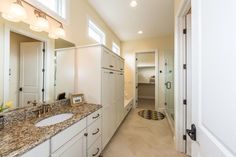 a large bathroom with marble counter tops and white cabinetry, along with a walk in shower