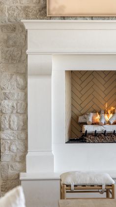 a fire place in the middle of a living room with white furniture and stone walls