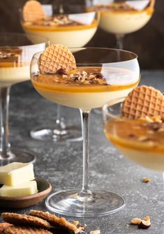 three glasses filled with desserts on top of a table next to crackers and cheese