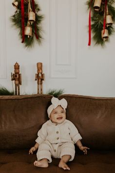 a baby sitting on top of a brown couch next to christmas wreaths and bells