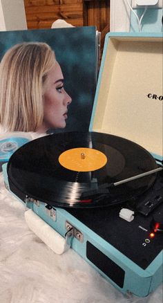 a record player sitting on top of a bed next to a box with an album