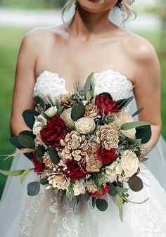 a bride holding a bouquet of red and white flowers on her wedding day in the park