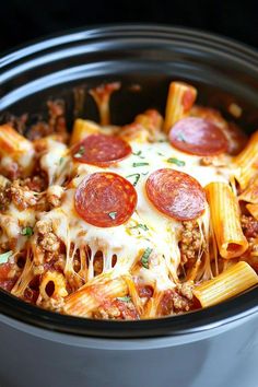 a crock pot filled with pasta and cheese topped with pepperoni pizza toppings