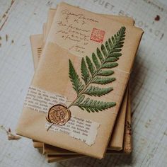 a stack of old envelopes with a wax stamp and fern leaf on them, sitting on top of a wooden table