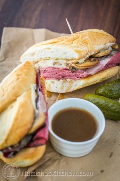 a roast beef sandwich with pickles and dipping sauce