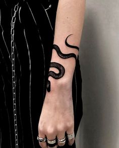 a woman's hand with a snake tattoo on her left arm and two rings around the wrist