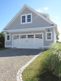 a large gray house with white trim on the front and side windows, along with a gravel driveway leading up to it