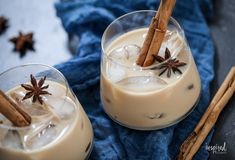 two glasses filled with anise and cinnamon on top of a blue towel next to cinnamon sticks