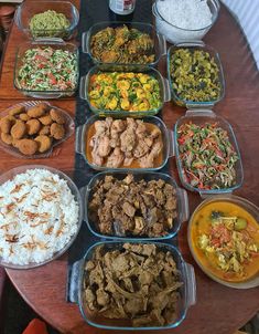 a wooden table topped with lots of different types of food and dishes filled with rice