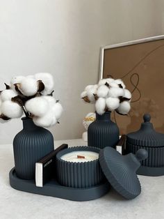 three black vases with cotton in them on a white counter top next to a mirror