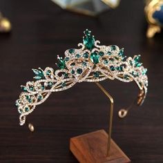 a tiara with green and white stones is on a wooden stand in front of a mirror