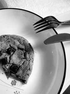 a piece of chocolate chip cookie on a plate with a fork and knife next to it