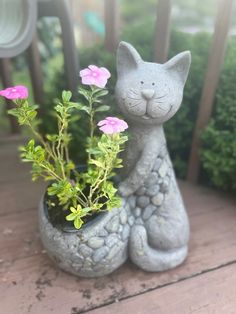 a cat statue sitting on top of a wooden table next to flowers and plants in a vase