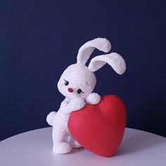 a stuffed rabbit holding a red heart on a white table against a dark blue background