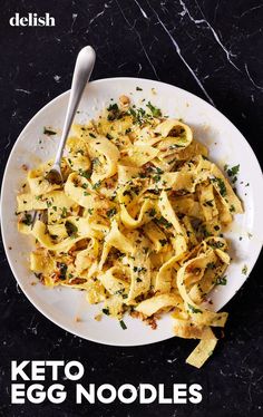 a white plate topped with pasta covered in cheese and parsley next to a spoon