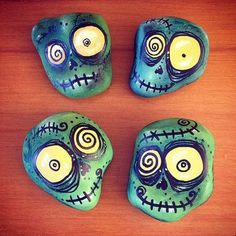 three painted rocks sitting on top of a wooden table with eyes in the shape of skulls