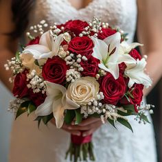 a bride holding a bouquet of red roses and white lilies on her wedding day