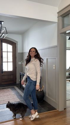 a woman standing next to a dog in a living room with hardwood floors and walls