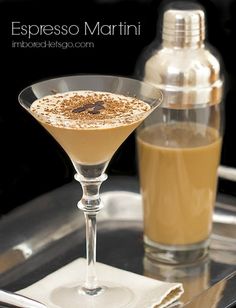 an espresso martini in a coupe glass on a tray next to a bottle