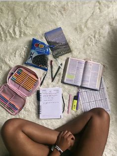 a woman is sitting on the floor with her legs crossed and books, pens, pencils, and other items