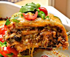 a slice of lasagna being lifted from a casserole dish with tomatoes and green peppers