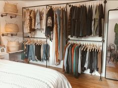 a bedroom with clothes hanging on racks and a bed in the foreground, next to a mirror