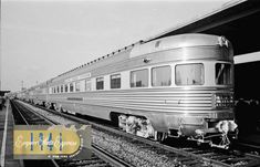 an old photo of a silver train on the tracks in front of a station platform