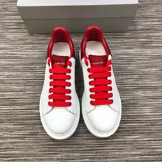 a pair of white and red sneakers on top of a carpeted floor next to a box