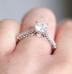 a close up of a person's hand holding a ring with a diamond on it