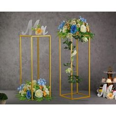 two tall gold vases with flowers in them and one on the floor next to each other