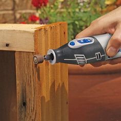 a person using a power drill to attach a wooden fence post with flowers in the background