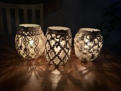 three lit candles sitting on top of a wooden table next to a vase with an intricate design