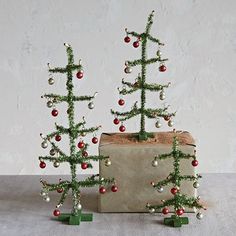 two small christmas trees sitting next to each other on top of a box with ornaments