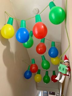 christmas lights hanging from the ceiling with elf on ladder next to them and an elf holding a green box